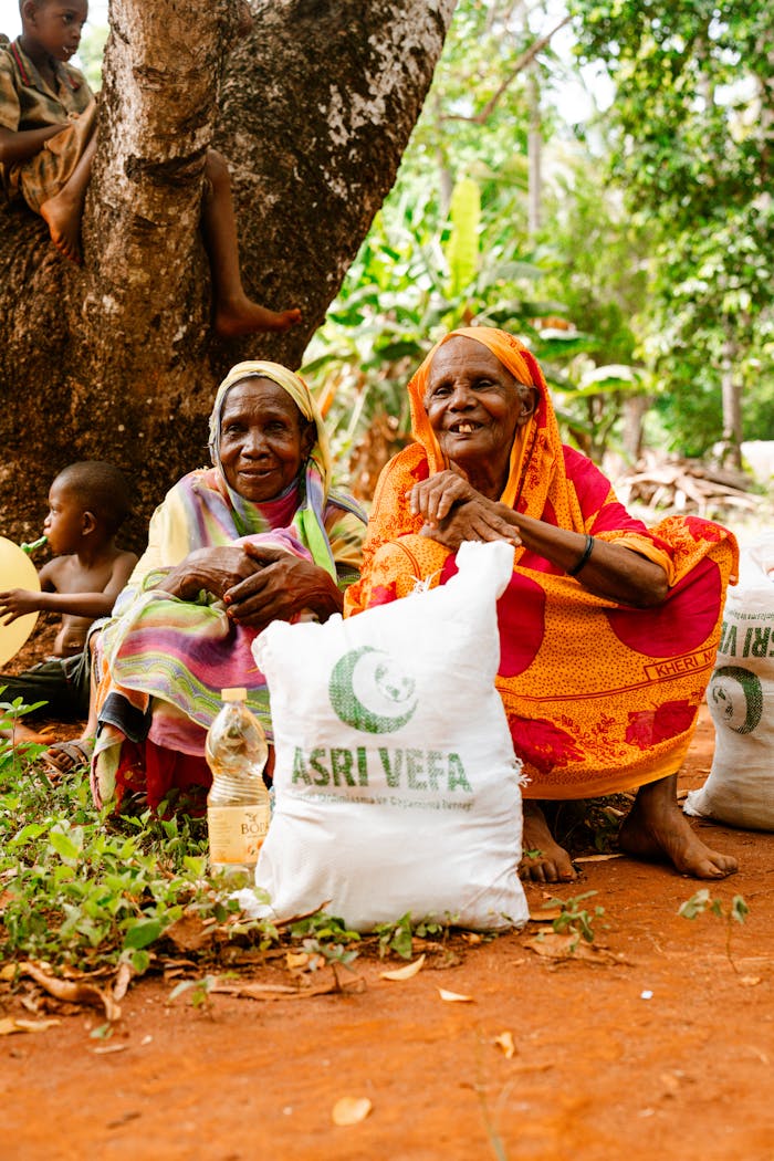 Two elderly women sitting outdoors with food aid bags, smiling and enjoying the sunny day.
