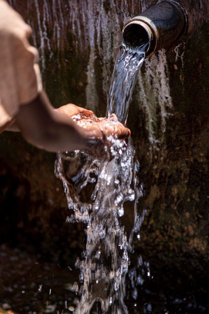 Close-up of hands collecting flowing water from a pipe outdoors.