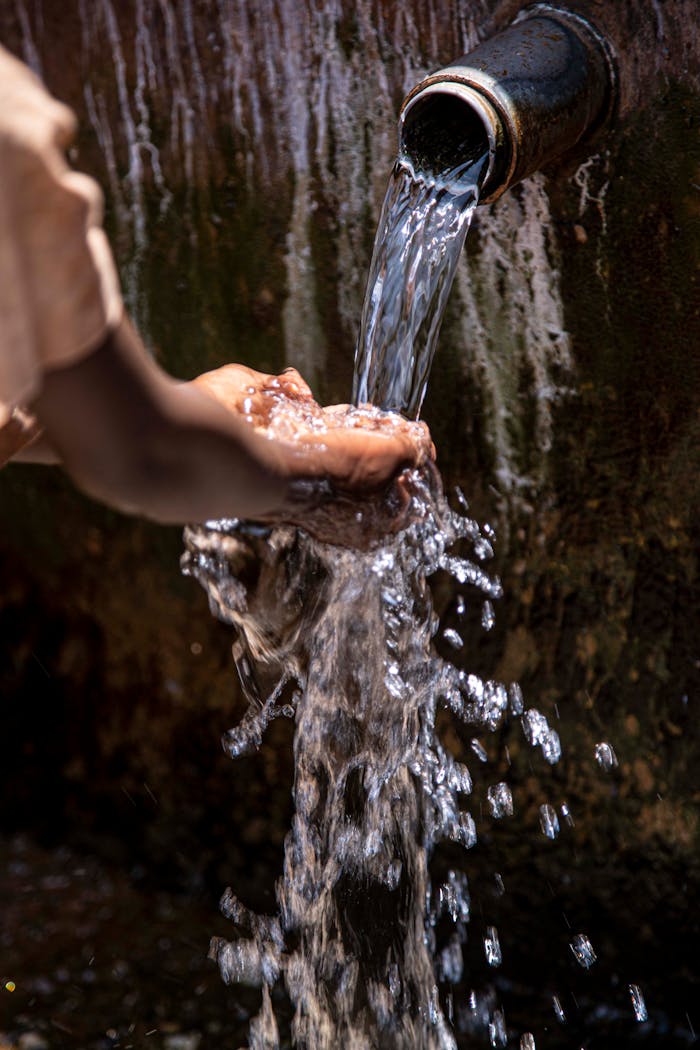 Hands catching fresh flowing water from an outdoor tap, emphasizing cleanliness and purity.