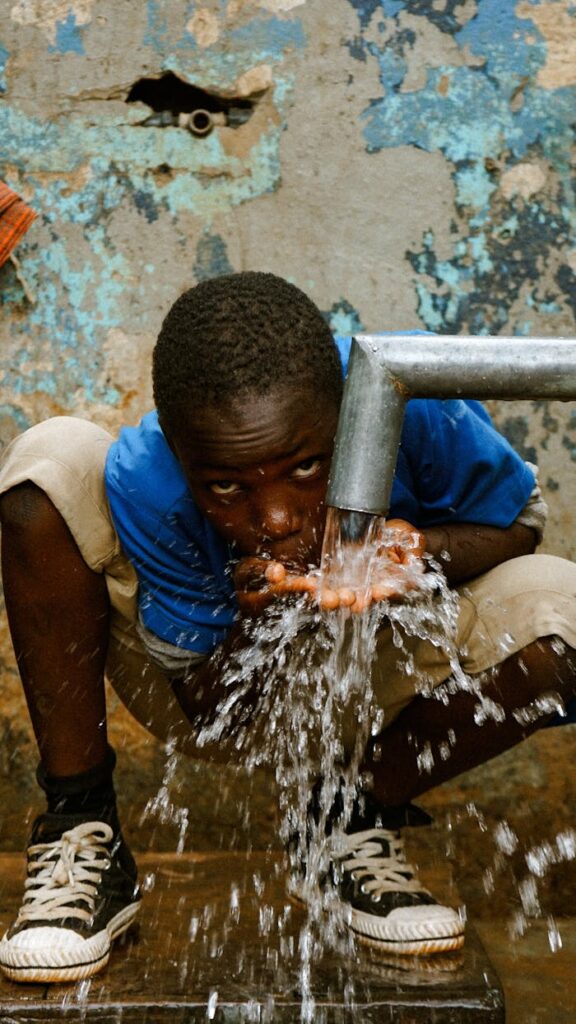 Young boy drinks water from a tap in a rustic setting.